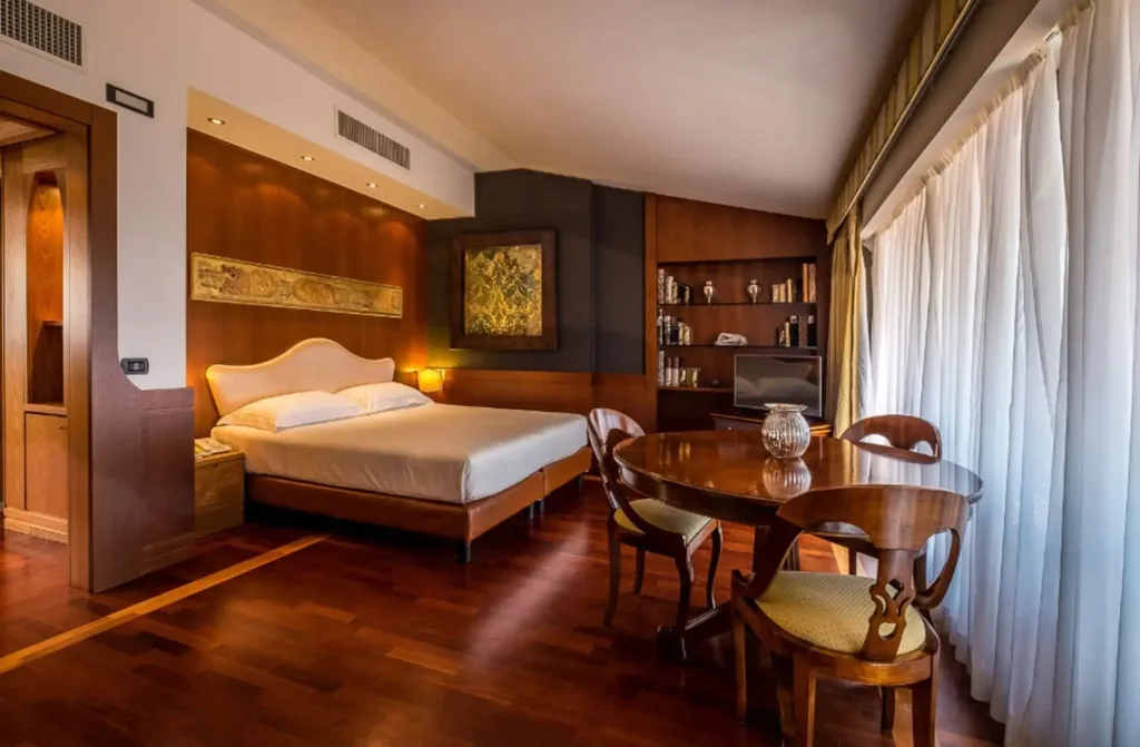 Suite elegante con letto matrimoniale, testiera bianca, tavolo da pranzo e grande finestra