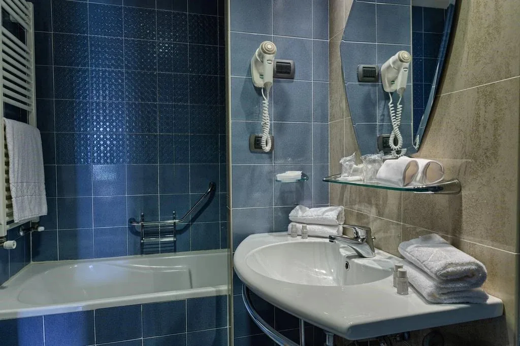 Bagno con piastrelle blu, vasca, lavabo e specchio con asciugacapelli