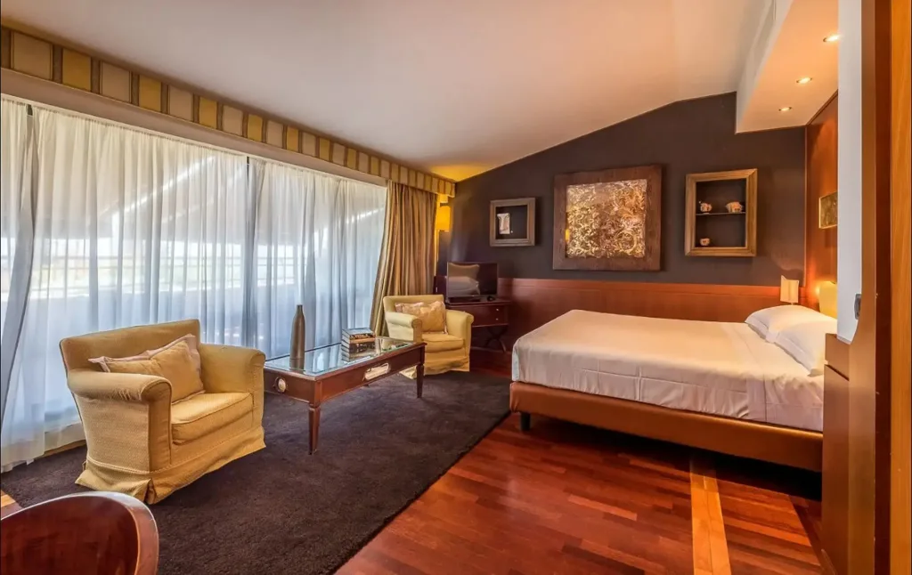 Suite luminosa con letto matrimoniale, poltrone, ampia vetrata e parete grigia decorata