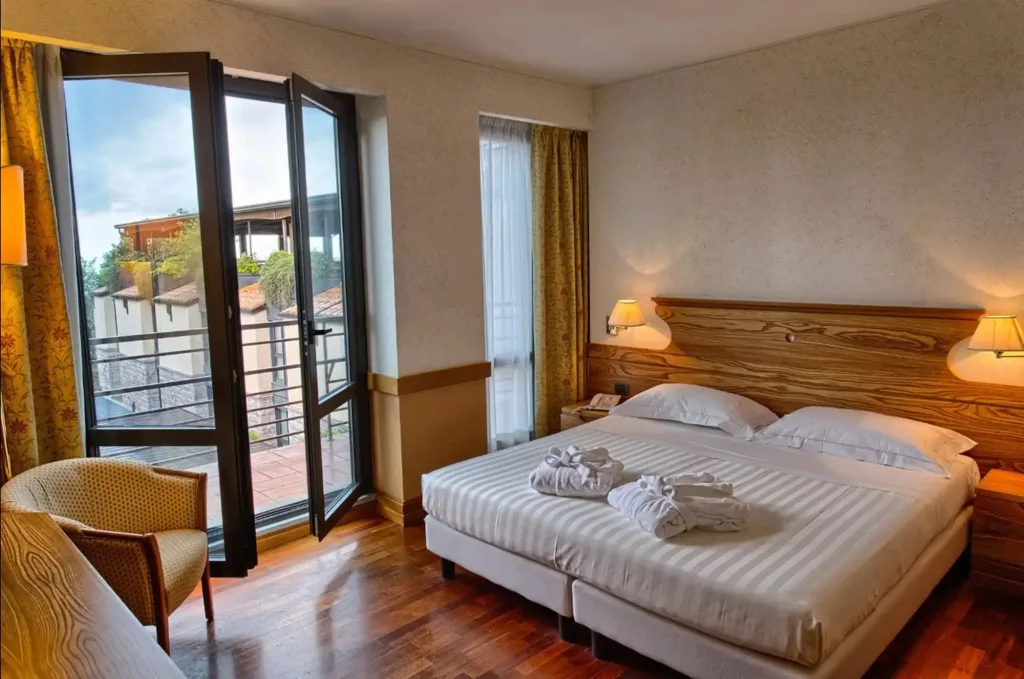Camera matrimoniale con accappatoi sul letto, porta finestra aperta sul balcone
