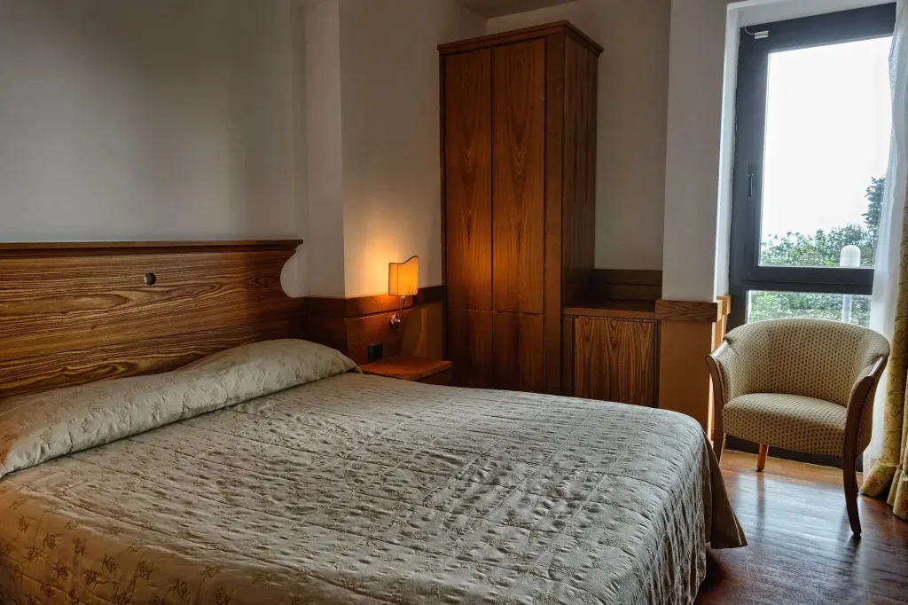 Camera con letto matrimoniale, armadio in legno e poltrona accanto alla finestra