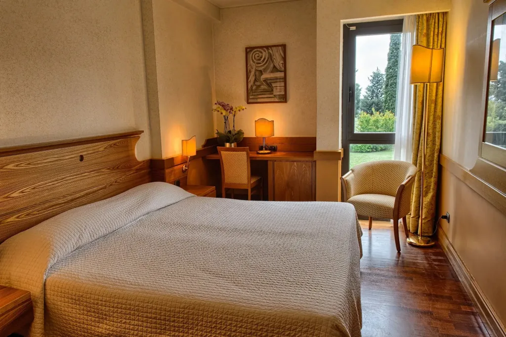 Camera con letto matrimoniale, scrivania con orchidea e porta finestra con vista sul giardino