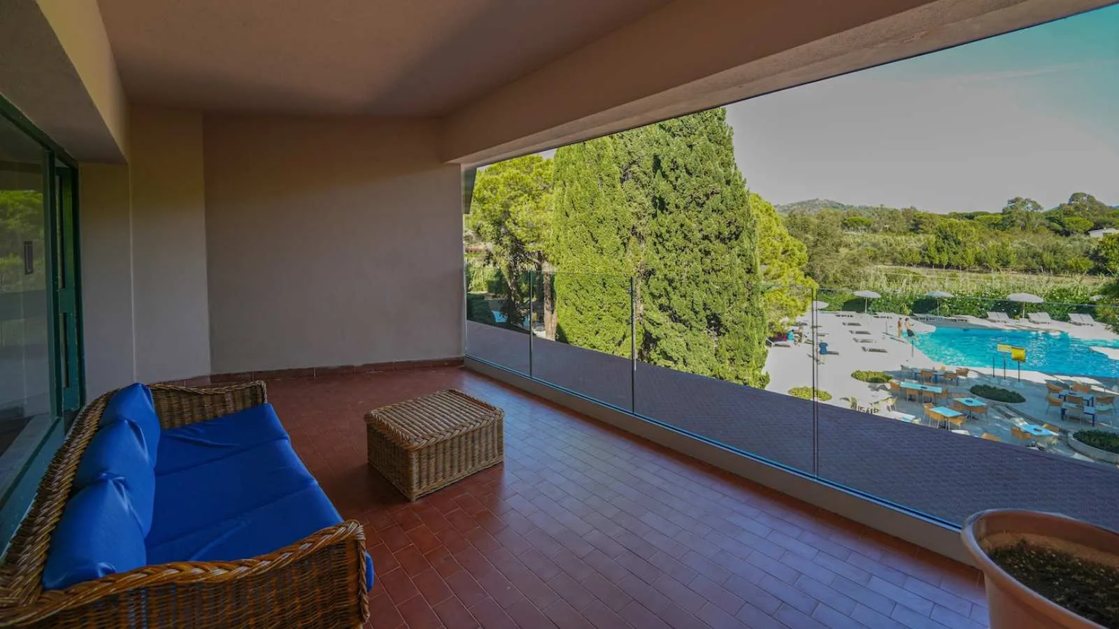 Terrazza coperta di TH Lacona con divano in vimini e vista sulla piscina e sul giardino.