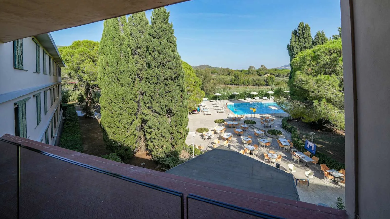 Veduta dalla terrazza di TH Lacona verso il giardino, i tavoli all’aperto e la piscina.