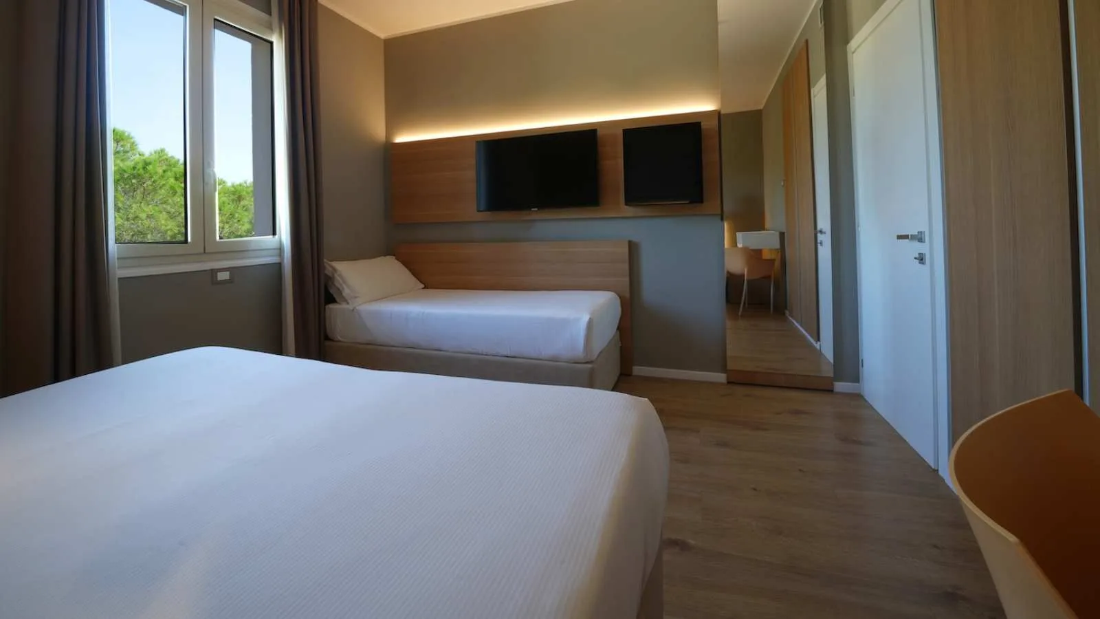 Camera di TH Lacona con letto matrimoniale, letto singolo vicino alla finestra e televisore a parete.