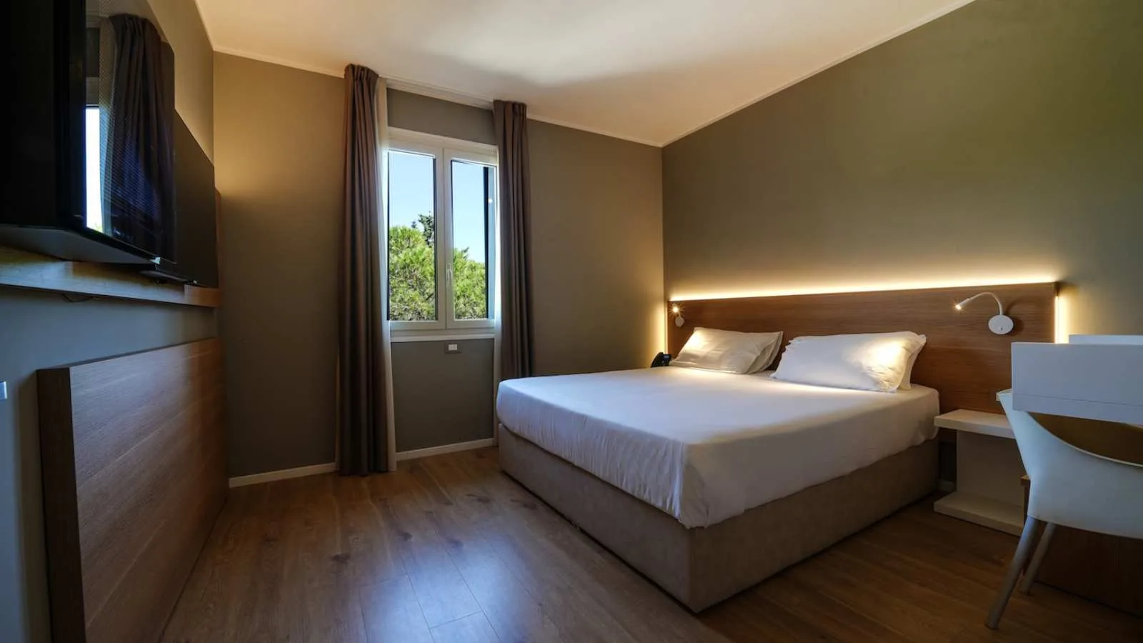 Interno di camera matrimoniale di TH Lacona con scrivania, TV e finestra sul verde.