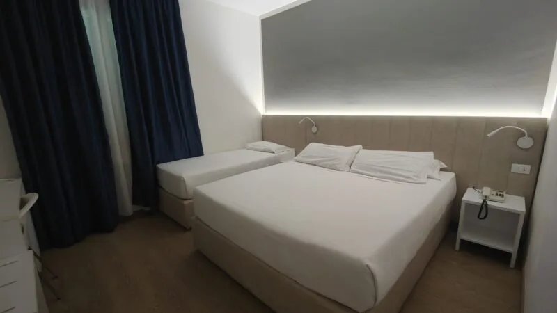 Interno di una camera di TH Lacona con letto matrimoniale e letto singolo, comodino e telefono.