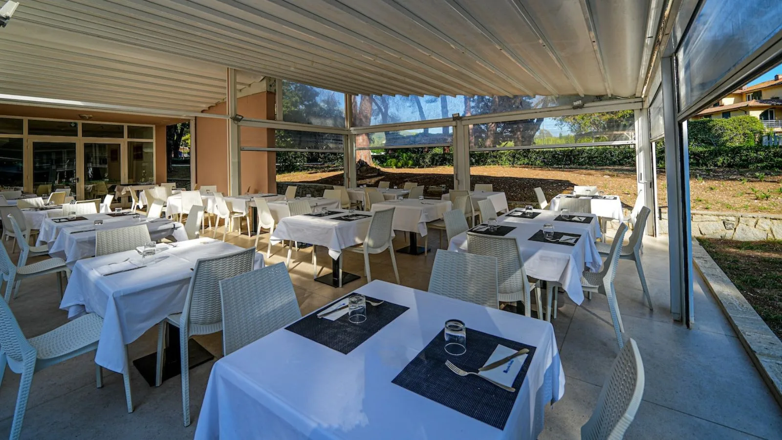 Veranda luminosa del ristorante di TH Lacona, con tavoli apparecchiati e vista sul giardino.