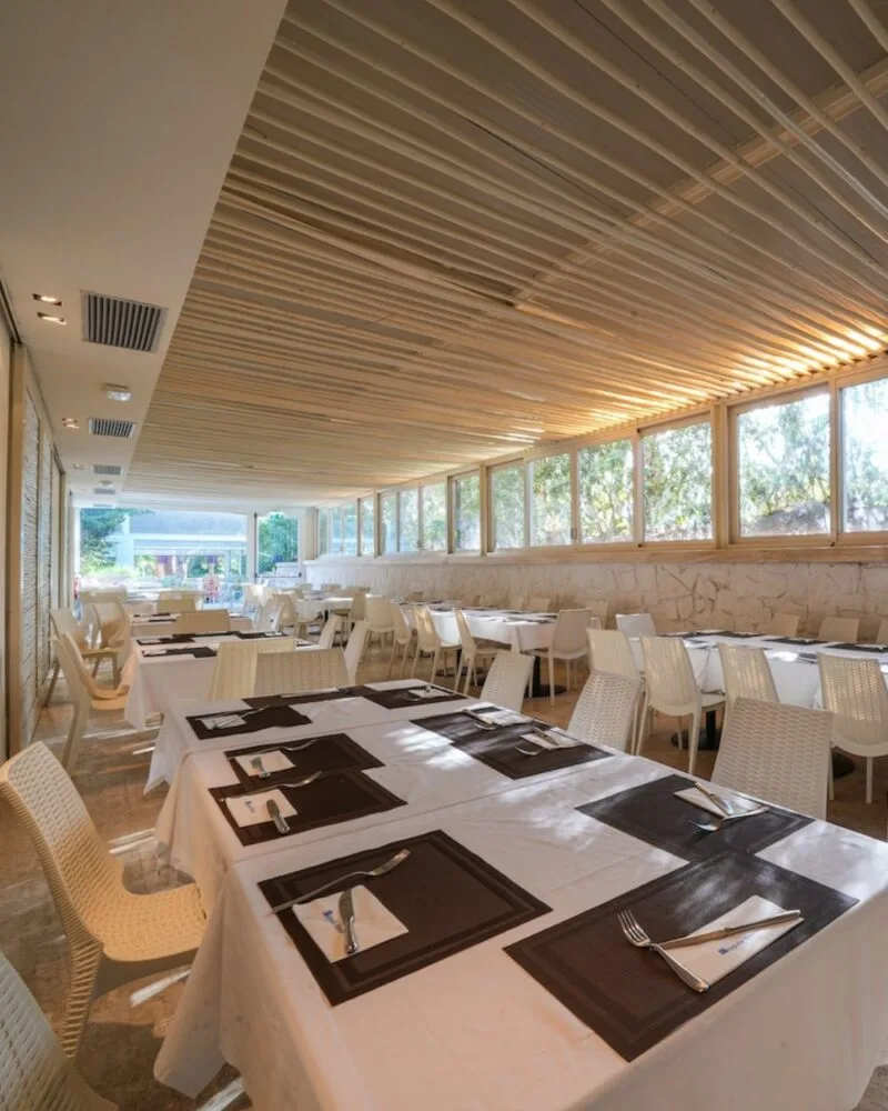 Sala del ristorante di TH Lacona con tavoli apparecchiati, ampie vetrate e affaccio sul verde.
