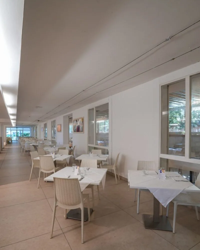 Sala interna del ristorante di TH Lacona con tavoli apparecchiati e sedie bianche.