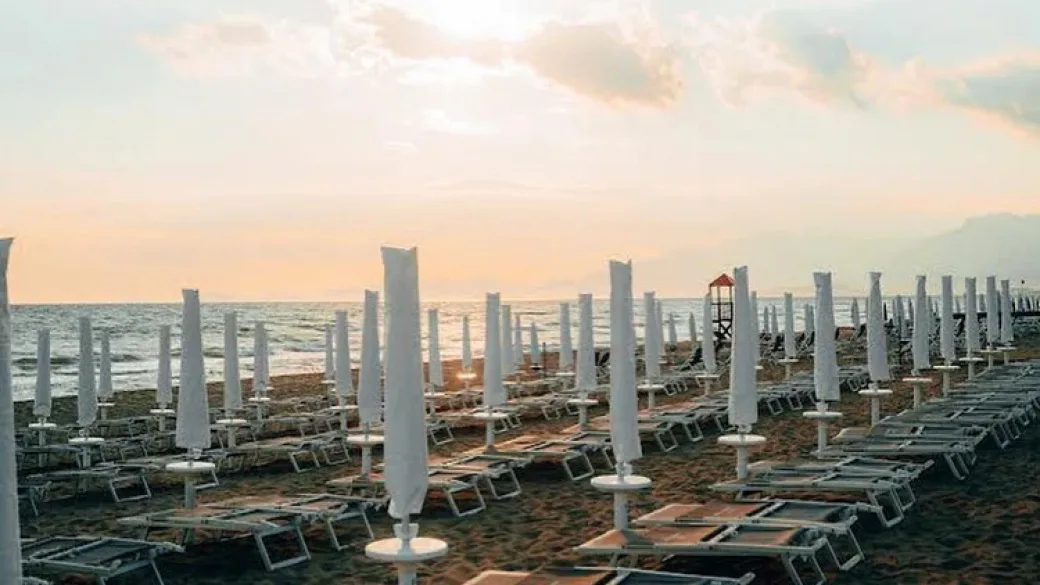 Spiaggia al tramonto con file di lettini e ombrelloni chiusi affacciati sul mare
