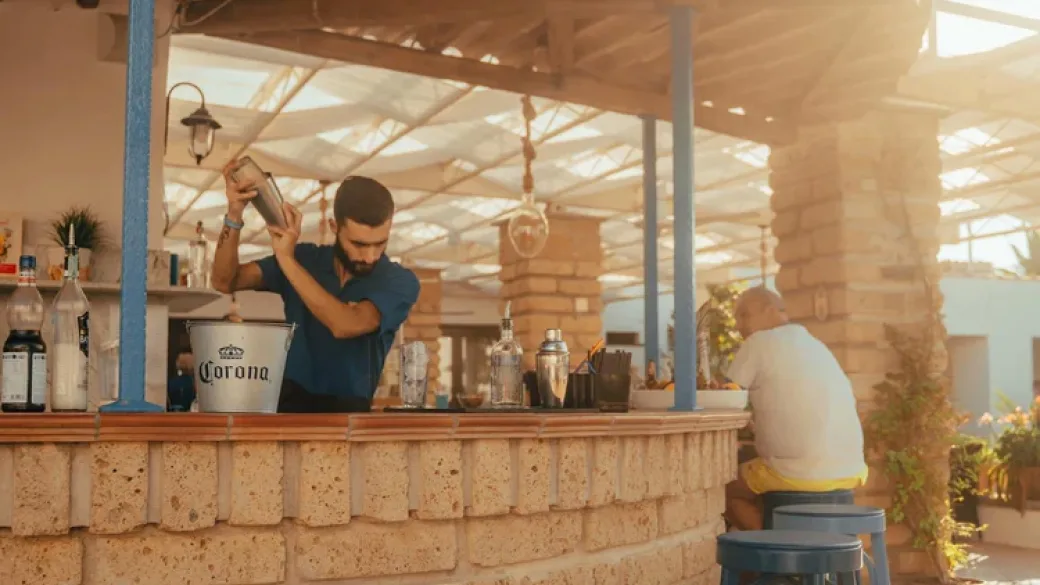 Barman prepara cocktail con shaker presso il bar all'aperto in pietra al tramonto