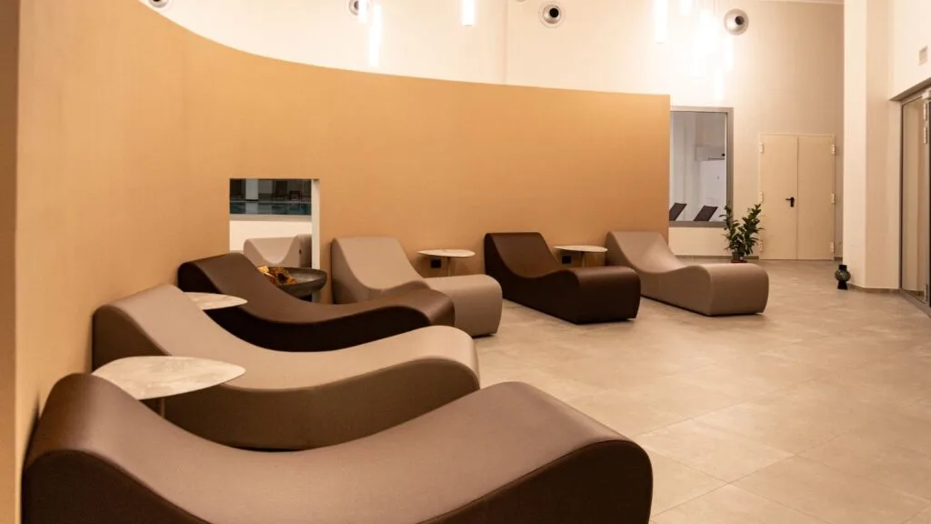 Sala d'attesa con sedili color crema e marrone, luci moderne e pareti beige, decorata con piante e oggetti minimalisti.