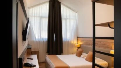 Camera da letto moderna con letto, finestre con tende bianche e scure, e parete con pannello di legno.