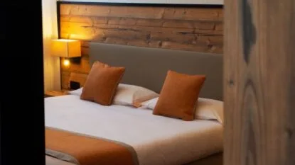 Letto king size con cuscini marroni e lampada accesa su parete di legno in camera.