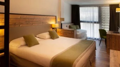 Camera moderna con letto, divano, scrivania e grande finestra con tende, atmosfera accogliente e luminosa.