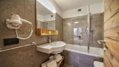 Bagno moderno con pareti in piastrelle marroni, lavabo sospeso, specchio e doccia con porta di vetro.