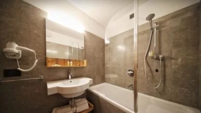 Bagno moderno con vasca, specchio e asciugacapelli, pareti rivestite di piastrelle marroni.
