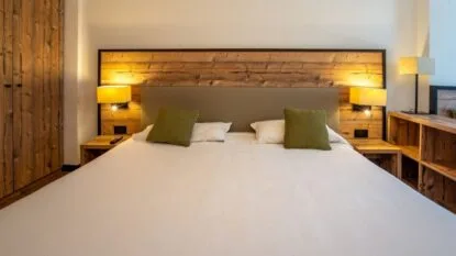 Letto matrimoniale con cuscini verdi, lampade accese e pareti in legno in una stanza accogliente.