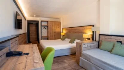 Camera d'hotel con letto matrimoniale, poltrona e scrivania, arredamento in legno e illuminazione calda.