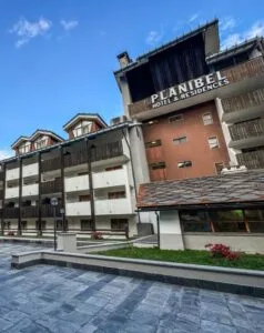 Hotel e residenze chiamato "Planibel" con balconi in legno e tetto in tegole, sotto un cielo blu.