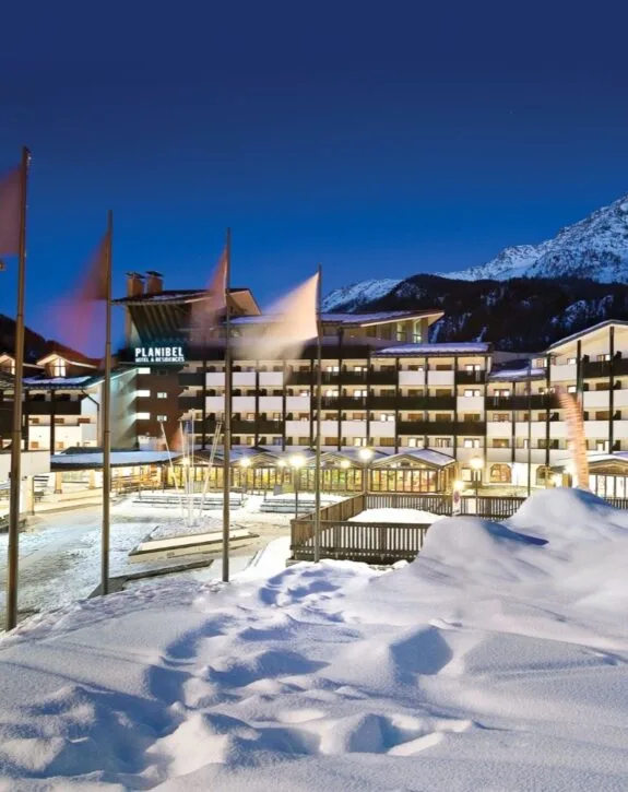 Hotel Planibel di notte con neve e montagne sullo sfondo.