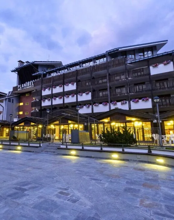 Edificio con balconi fioriti, illuminato di sera, sotto un cielo nuvoloso.