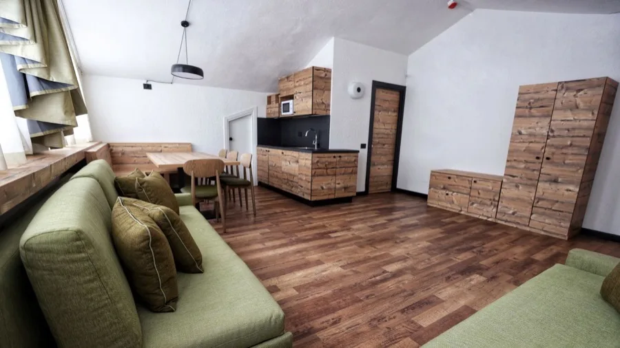 Interno di un appartamento con divani verdi, tavolo da pranzo, cucinino in legno e pareti bianche.
