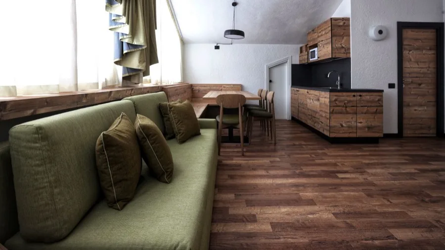 Soggiorno moderno con divano verde, tavolo in legno e angolo cottura in stile rustico.
