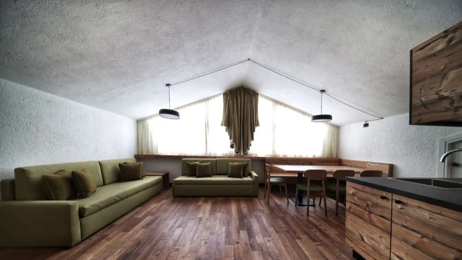 Interior di soggiorno con divani, tavolo, sedie, grandi finestre e pavimento in legno.