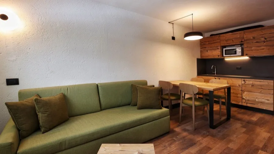 Interno di soggiorno con divano verde, tavolo da pranzo e cucina in legno.