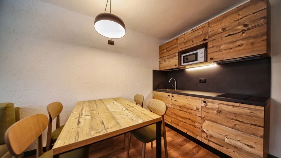Angolo cucina con armadietti in legno, piano di lavoro nero, tavolo in legno e sedie in stile moderno.