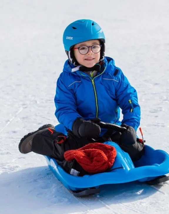 Bambino con casco e slittino sulla neve