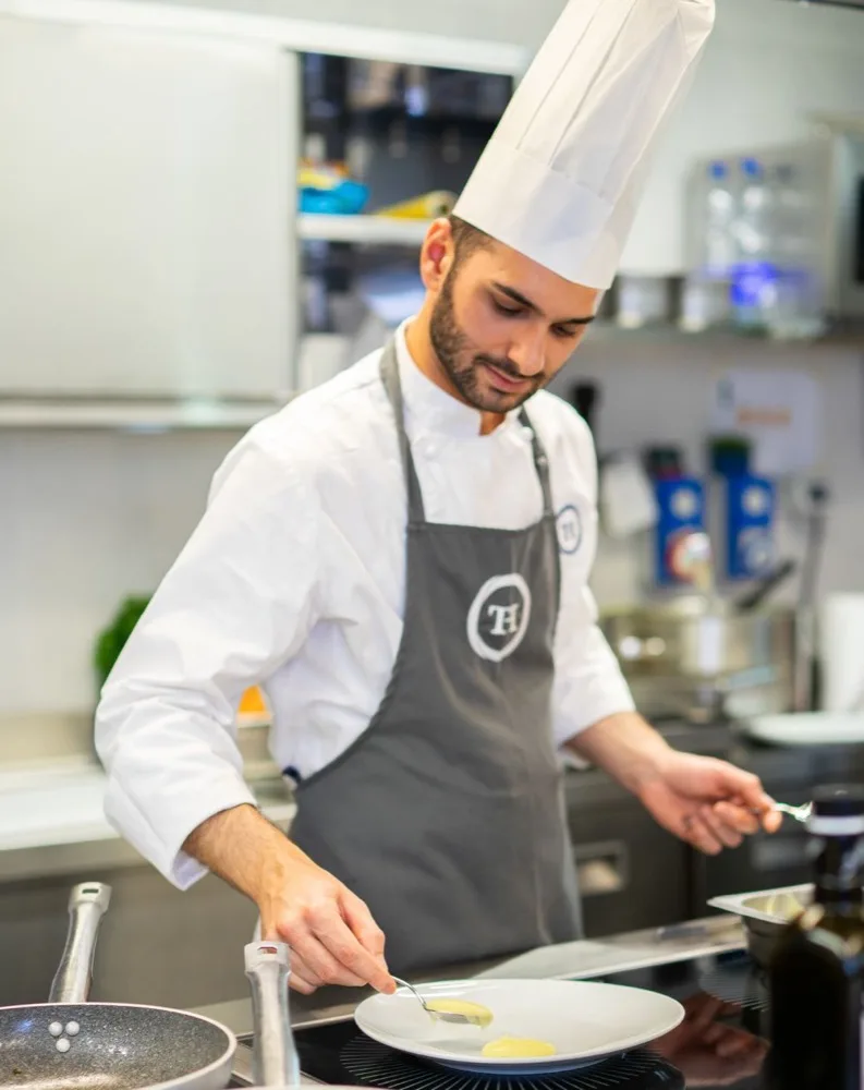 Chef in cucina che impiatta con cura una preparazione gastronomica