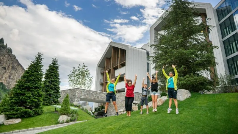 Famiglia con bambini che salta felice sul prato verde davanti all'hotel di montagna