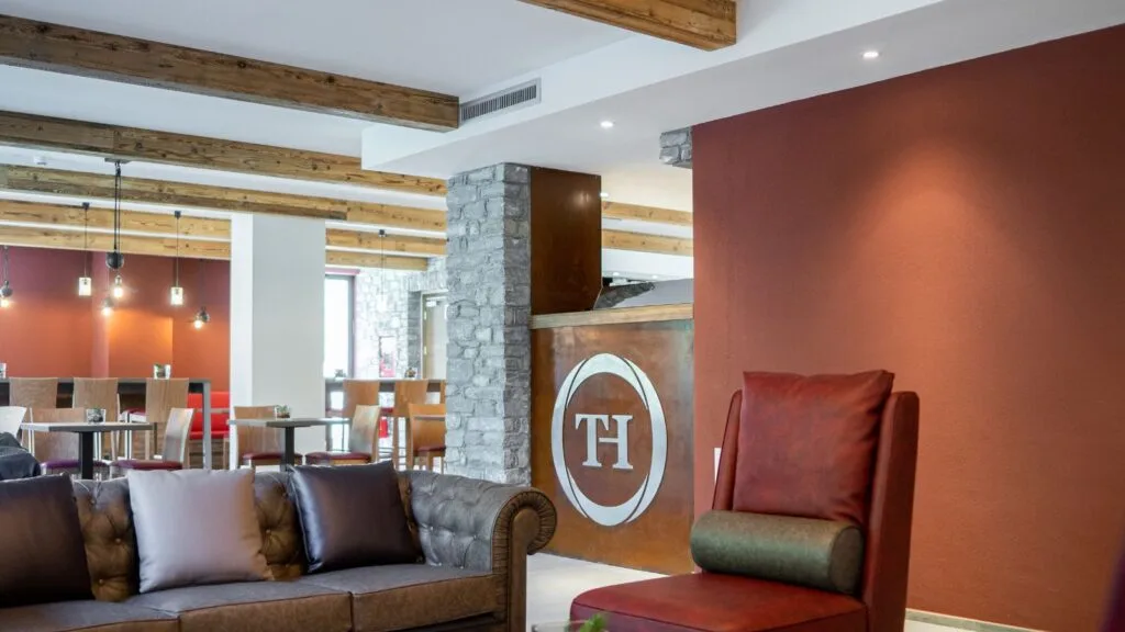Area lounge dell'hotel con divano in pelle, logo TH e sala ristorante sullo sfondo