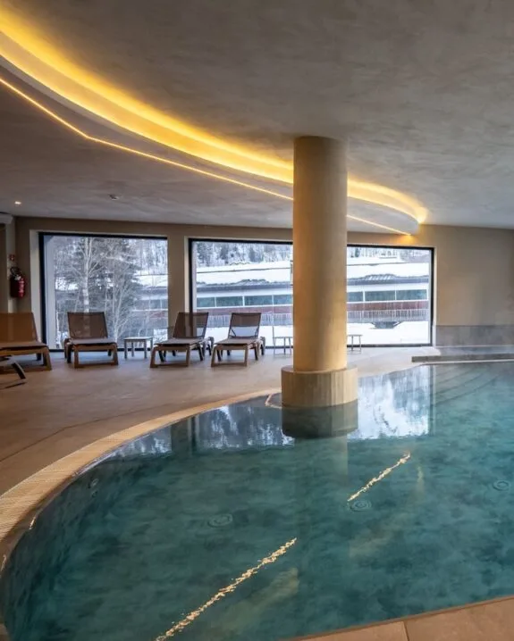 Piscina interna con lettini e grandi finestre affacciate sul paesaggio innevato
