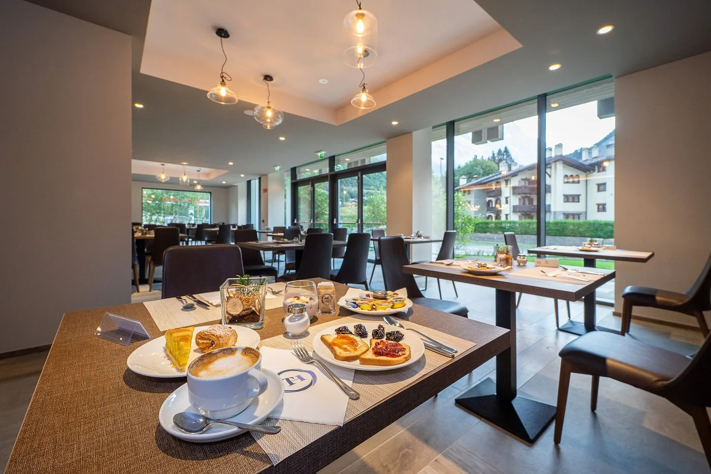 Tavolo della colazione con cappuccino, toast e dolci in sala luminosa con vista