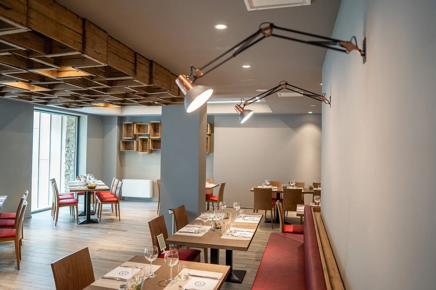 Sala ristorante moderna con tavoli apparecchiati, sedute rosse e soffitto decorato in legno