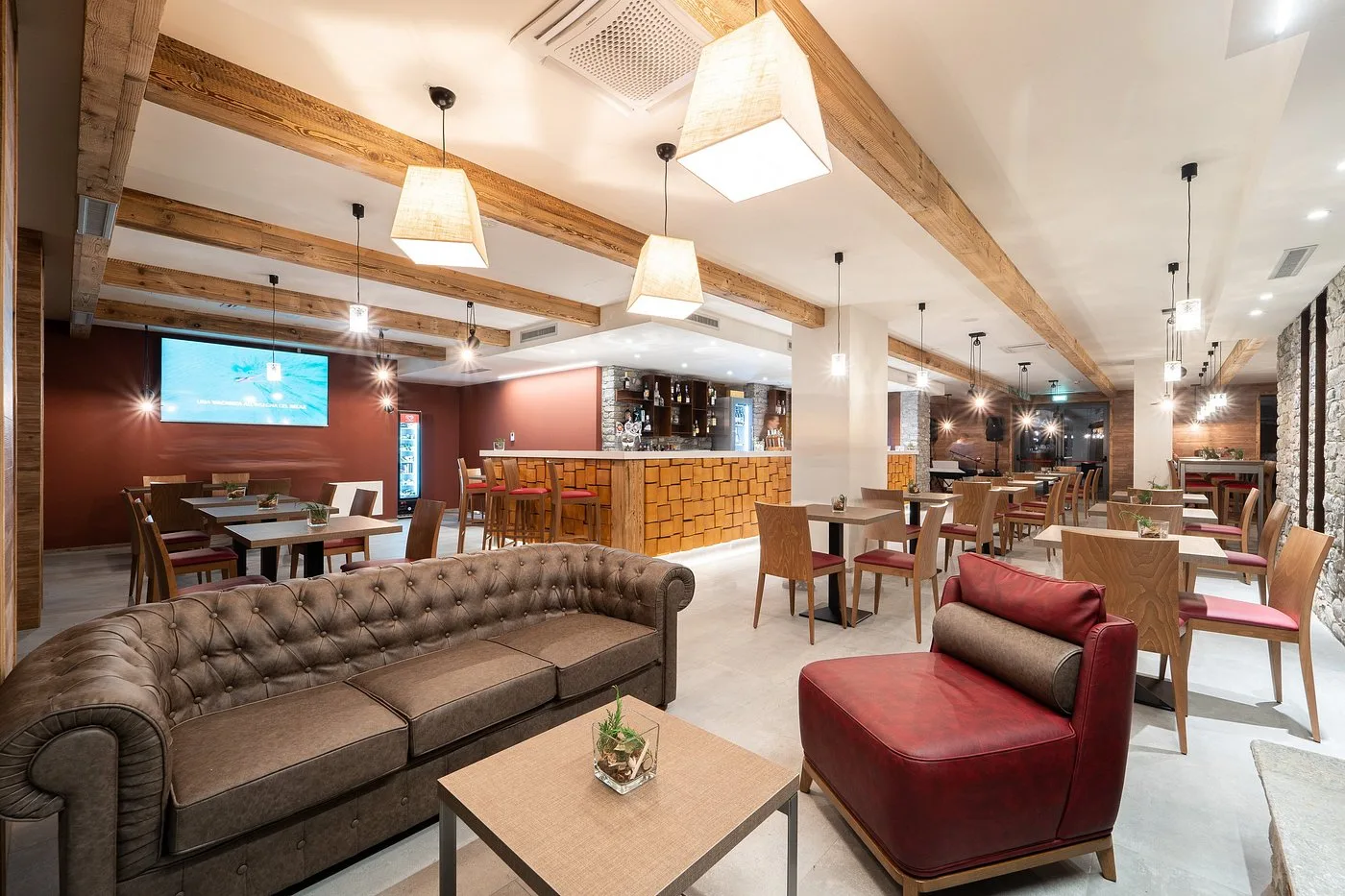 Area bar e lounge dell'hotel con divani in pelle, travi in legno e bancone illuminato
