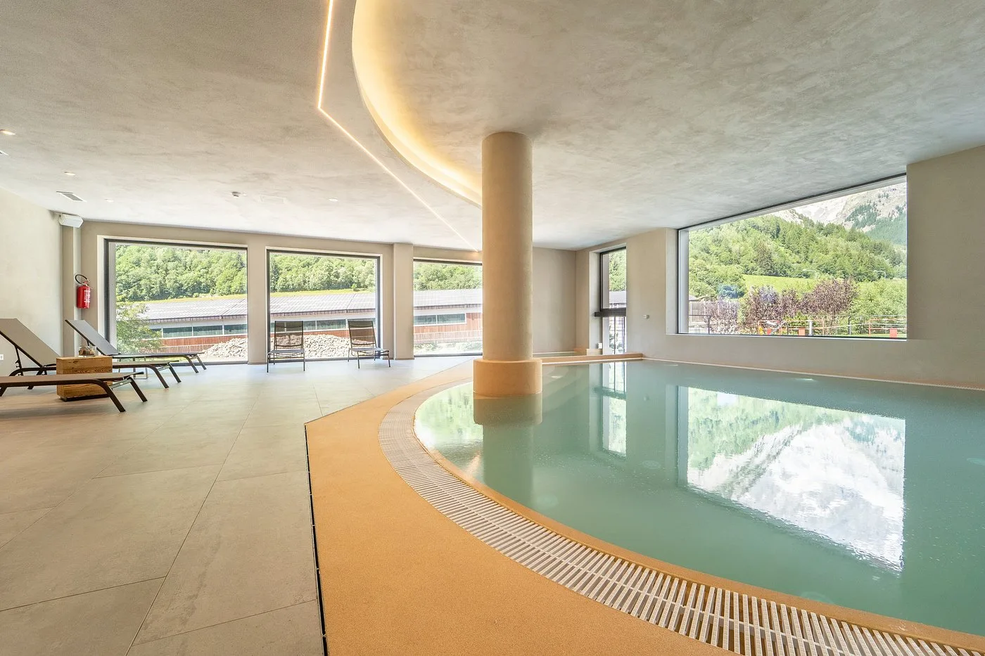Piscina coperta dell'hotel con ampie vetrate affacciate sul paesaggio montano estivo