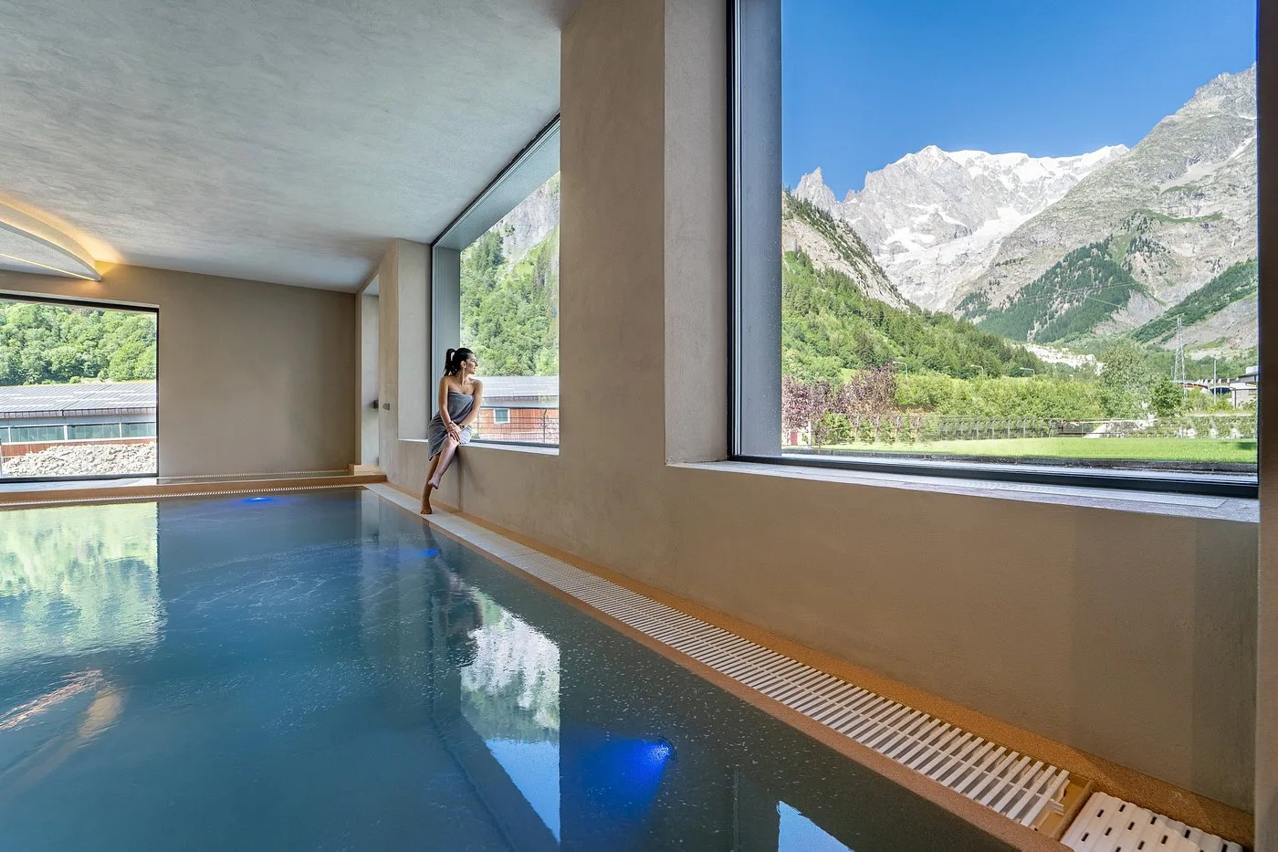 Donna seduta al bordo della piscina interna con vista sulle vette innevate del Monte Bianco