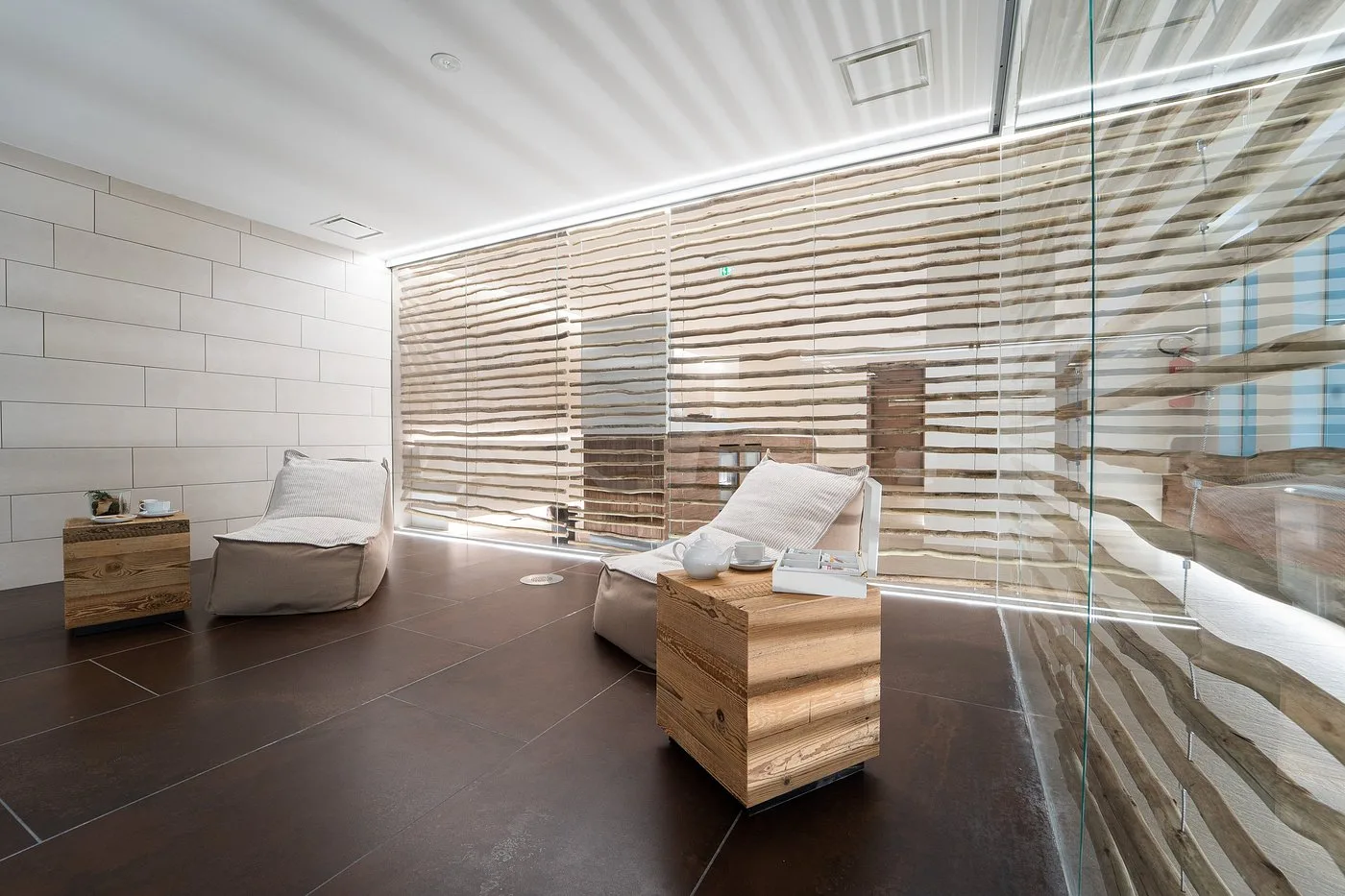 Area relax della spa con pouf, tavolini in legno e parete decorativa illuminata