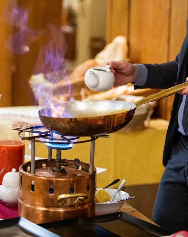 Persona che cucina flambé con padella su fornello a gas e fiamma blu in cucina.