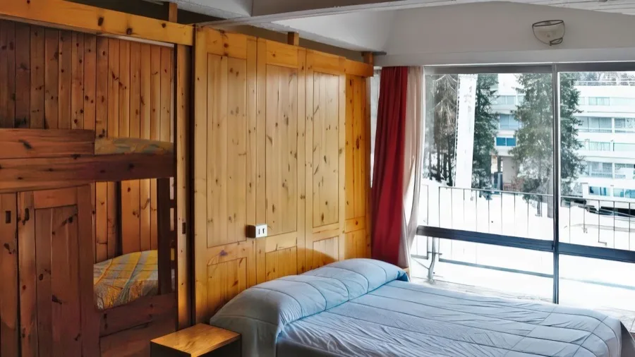 Camera da letto con letto matrimoniale, pareti in legno, armadio e grande finestra con vista esterna.