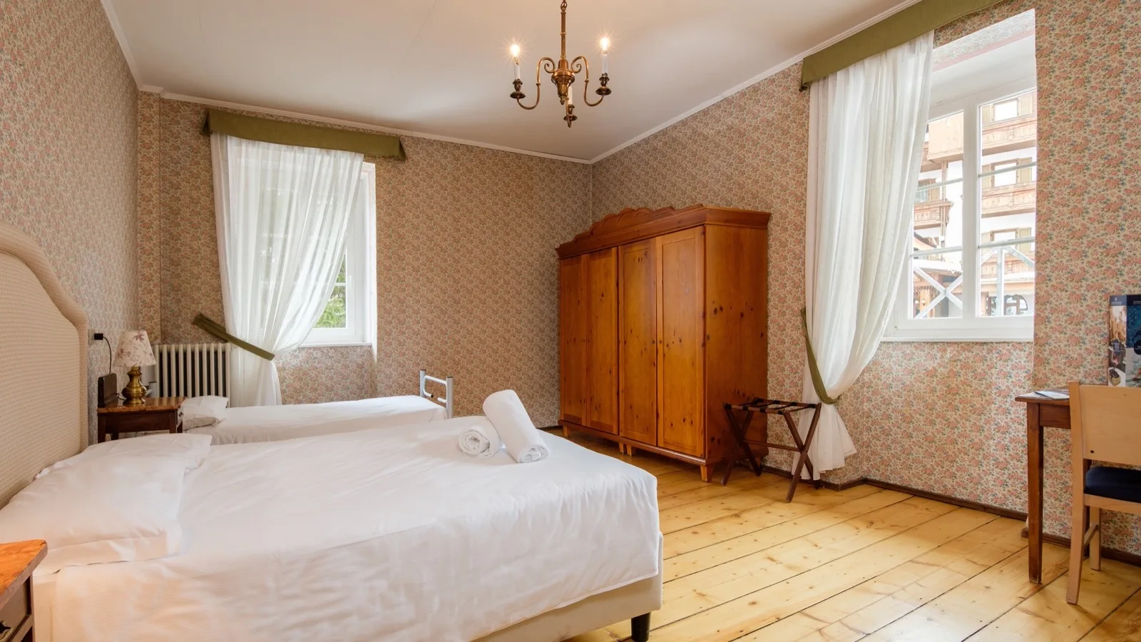 Camera da letto con due letti singoli, armadio in legno, pavimento in legno chiaro e tende bianche semi-trasparenti.
