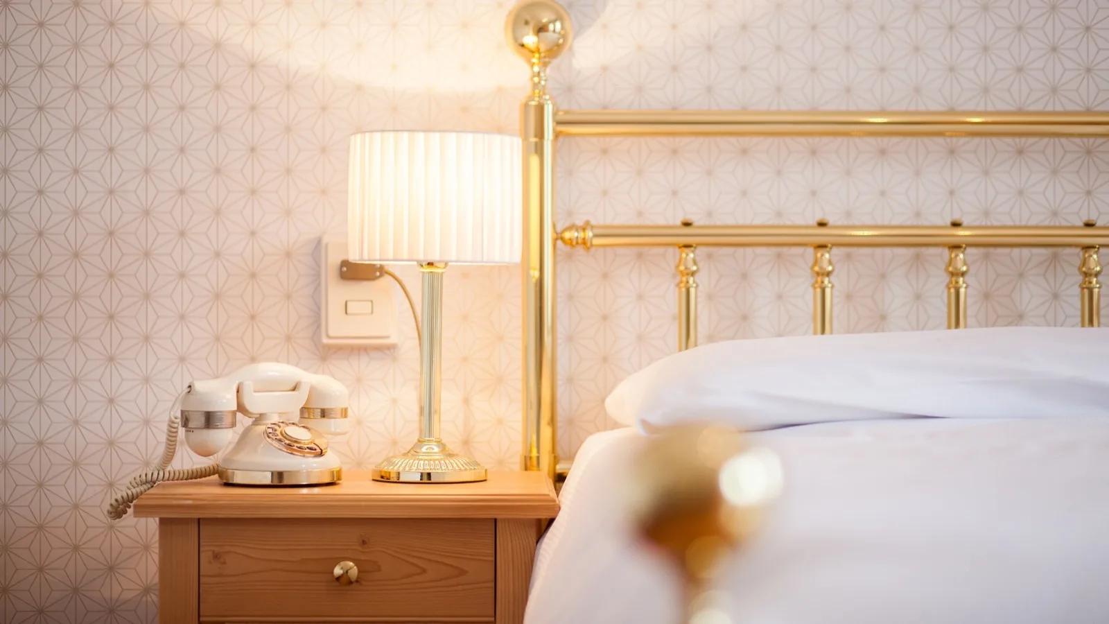 Comodino in legno con telefono vintage, lampada elegante e letto con testiera dorata in camera da letto.