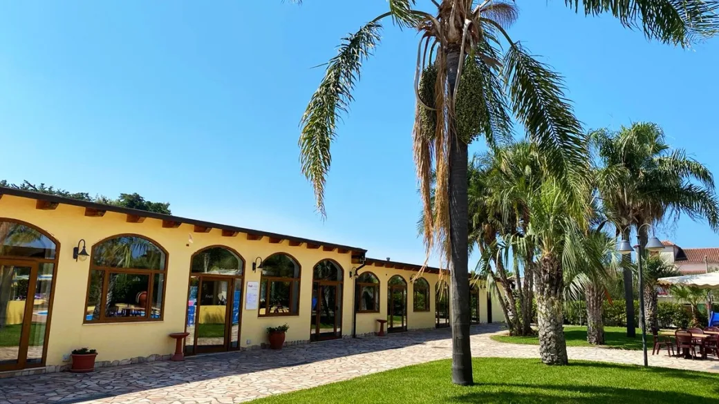 Edificio dell'hotel con ampie finestre ad arco, vialetto in pietra e palme nel giardino soleggiato
