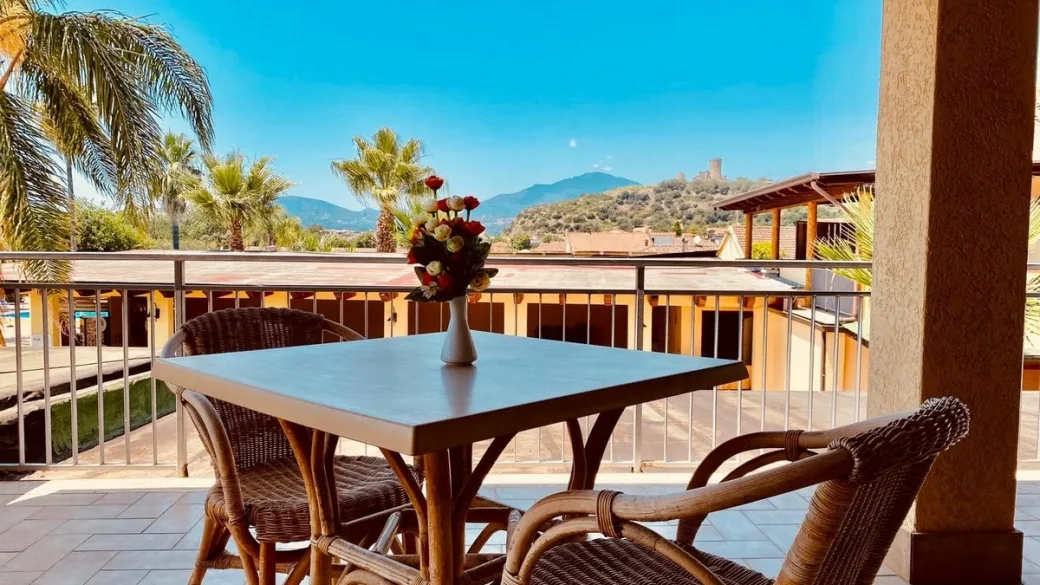 Terrazza con tavolo, sedie in vimini e vaso di fiori con vista panoramica su colline e torre