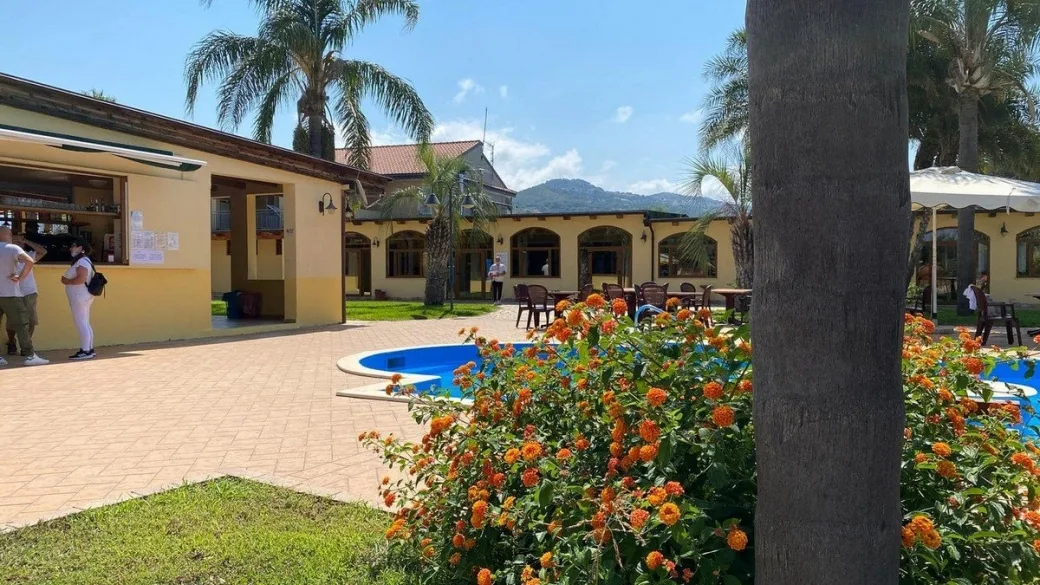 Area bar all'aperto con fiori arancioni, palme e piscina nel giardino dell'hotel